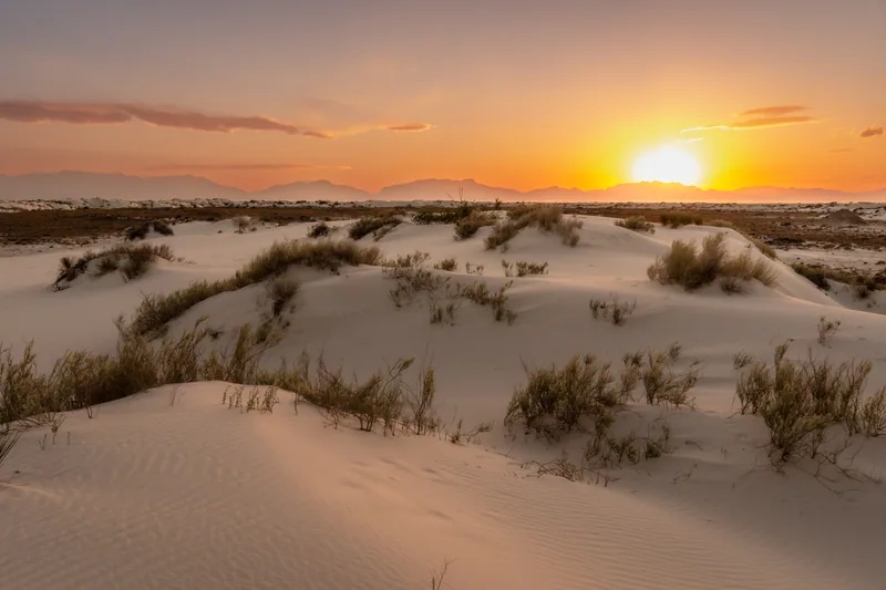 Soft evening light across white gypsum dunes and the distant mountains at White Sands
