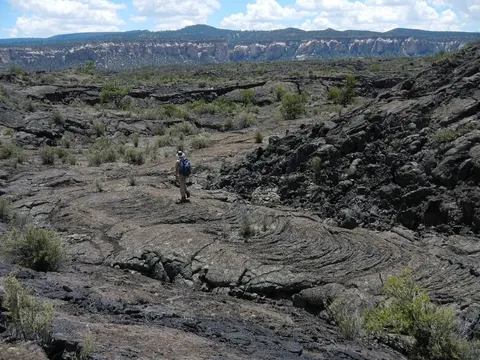 A hiker crossing the dark lava landscape at El Malpais