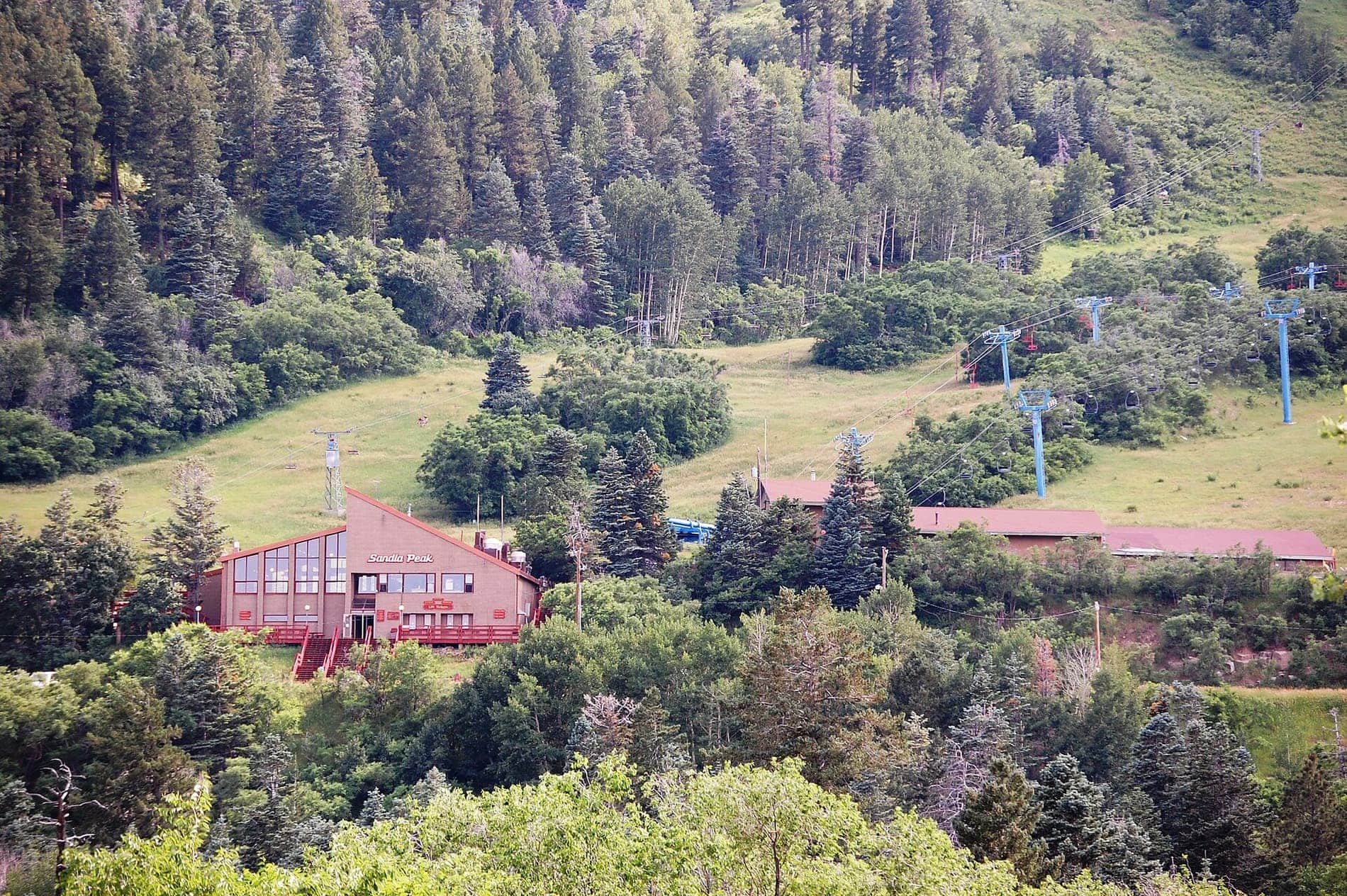 Summer view of the Sandia Peak Ski Area base lodge with chairlifts climbing the grassy slopes behind it